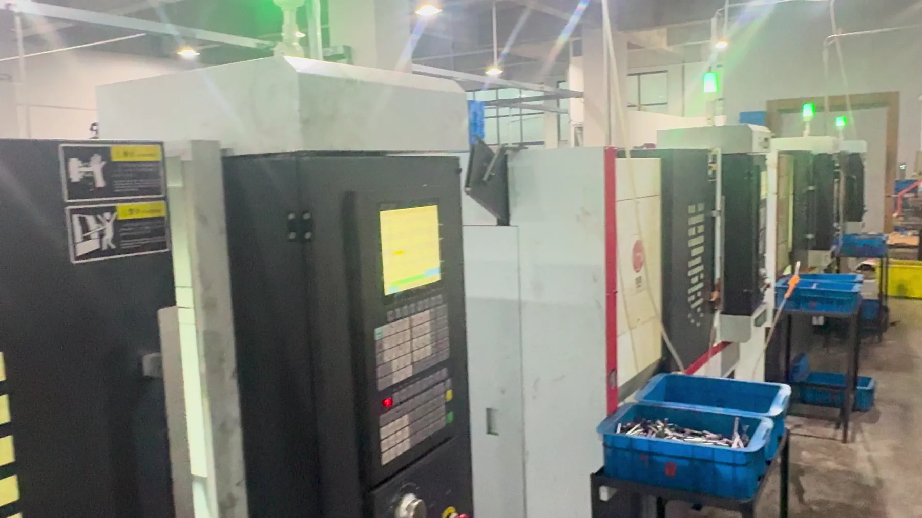 Real supplier workshop with a row of enclosed CNC machining cells and blue production bins